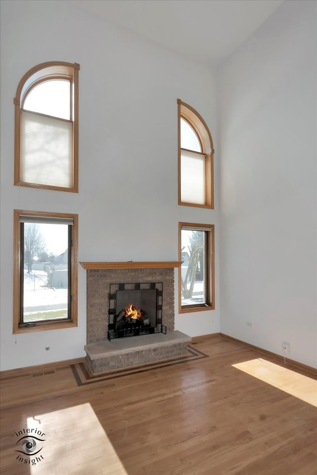 unfurnished living room featuring hardwood / wood-style floors, a fireplace, and a high ceiling