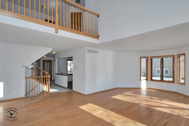 unfurnished living room featuring a towering ceiling and light hardwood / wood-style flooring