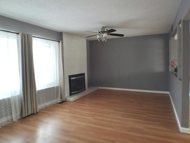 unfurnished living room featuring a tiled fireplace, ceiling fan, a textured ceiling, and light wood-type flooring