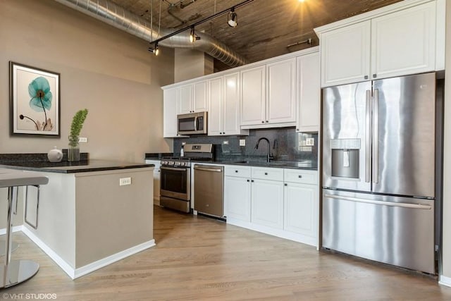 kitchen featuring rail lighting, white cabinetry, stainless steel appliances, and a high ceiling