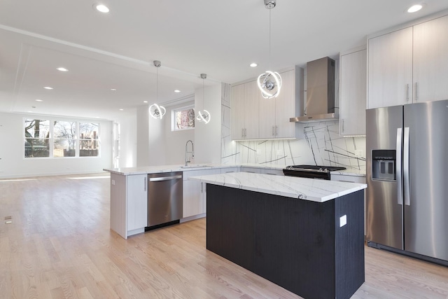 kitchen with sink, wall chimney exhaust hood, appliances with stainless steel finishes, decorative light fixtures, and kitchen peninsula