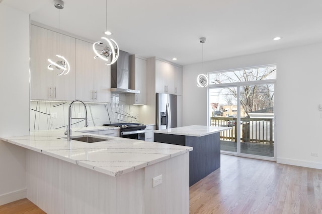 kitchen with pendant lighting, sink, wall chimney exhaust hood, kitchen peninsula, and stainless steel appliances