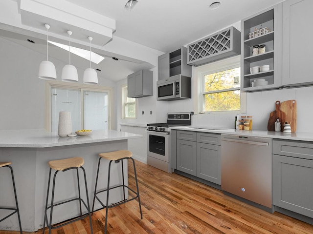 kitchen with a kitchen bar, gray cabinets, light hardwood / wood-style flooring, and stainless steel appliances