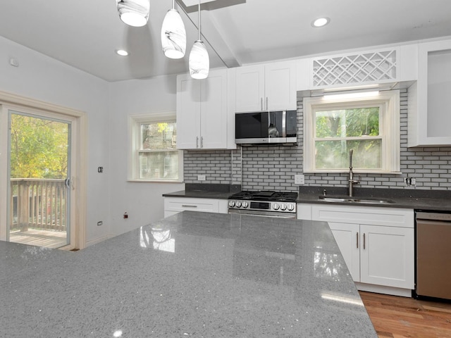 kitchen featuring dark stone counters, white cabinets, stainless steel appliances, and decorative light fixtures