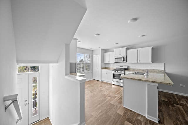 kitchen with sink, stainless steel appliances, tasteful backsplash, kitchen peninsula, and white cabinets