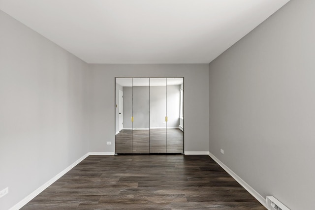 unfurnished bedroom featuring dark hardwood / wood-style floors, baseboard heating, and a closet