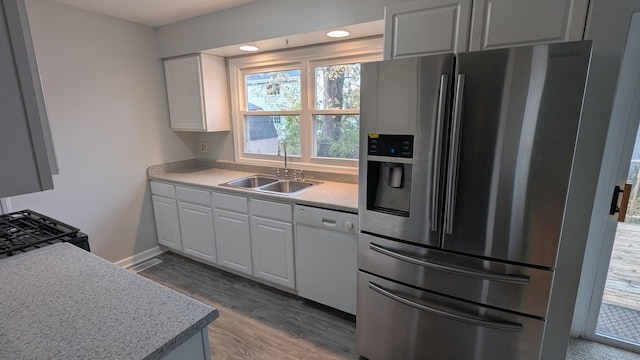 kitchen with black gas range oven, a sink, white cabinets, dishwasher, and stainless steel fridge