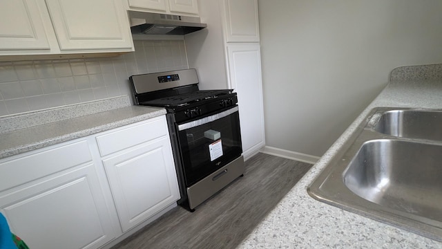 kitchen featuring tasteful backsplash, under cabinet range hood, light countertops, gas stove, and dark wood-style flooring