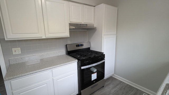 kitchen featuring baseboards, stainless steel gas range, under cabinet range hood, white cabinetry, and backsplash