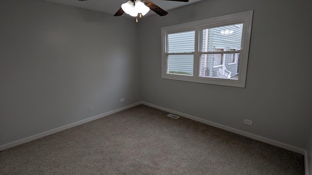 spare room featuring dark colored carpet, visible vents, baseboards, and a ceiling fan