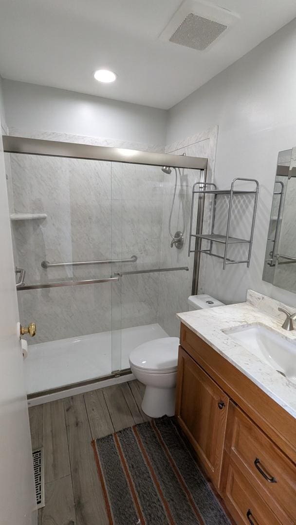 bathroom featuring visible vents, a shower stall, toilet, wood finished floors, and vanity