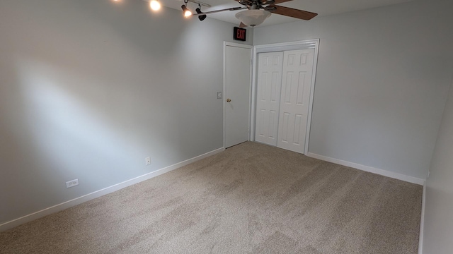 unfurnished bedroom featuring a closet, carpet, rail lighting, baseboards, and ceiling fan