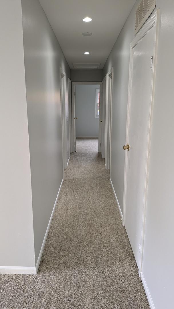 hallway featuring visible vents, baseboards, and carpet flooring