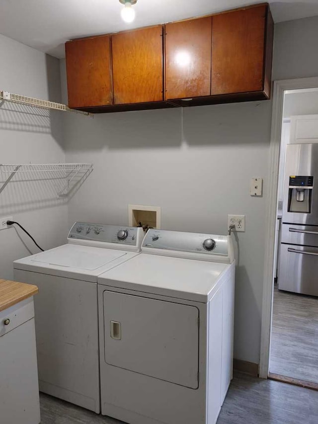 laundry area featuring washer and clothes dryer, cabinet space, and light wood-style floors