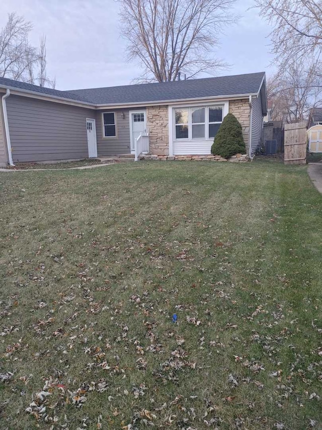 ranch-style home with stone siding, roof with shingles, a front lawn, and fence