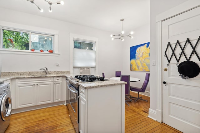 kitchen featuring stainless steel gas range oven, light wood-type flooring, decorative light fixtures, white cabinetry, and washer / clothes dryer