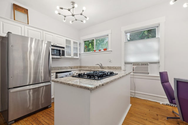 kitchen with light wood-type flooring, a notable chandelier, light stone counters, white cabinetry, and stainless steel appliances