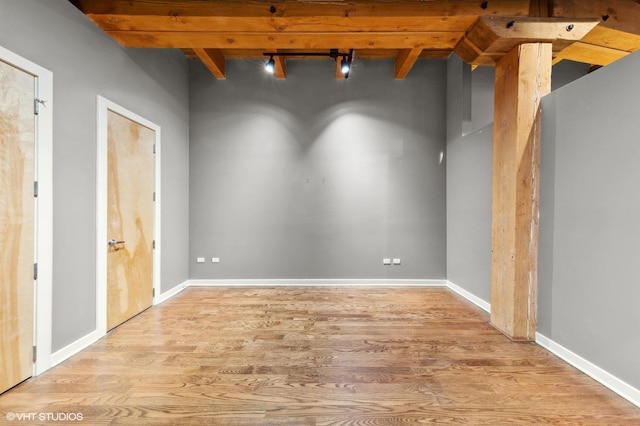 empty room featuring beam ceiling, light wood-type flooring, and rail lighting