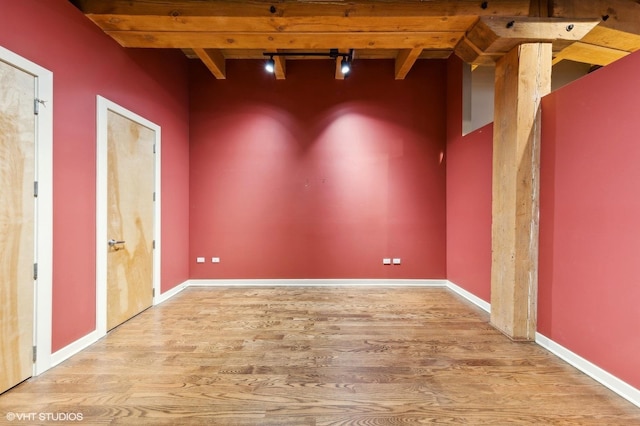 spare room featuring beam ceiling, wood-type flooring, and track lighting