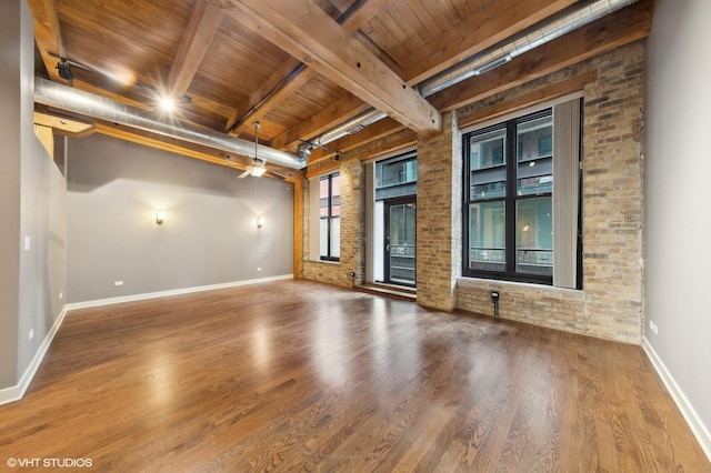 empty room with ceiling fan, beamed ceiling, brick wall, hardwood / wood-style floors, and wood ceiling