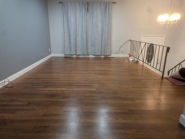 spare room with a notable chandelier, dark wood-style flooring, and baseboards