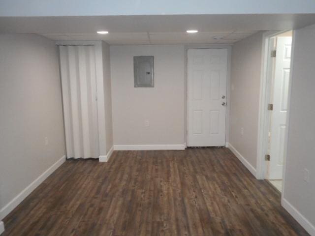 interior space with a drop ceiling, dark wood finished floors, electric panel, and baseboards