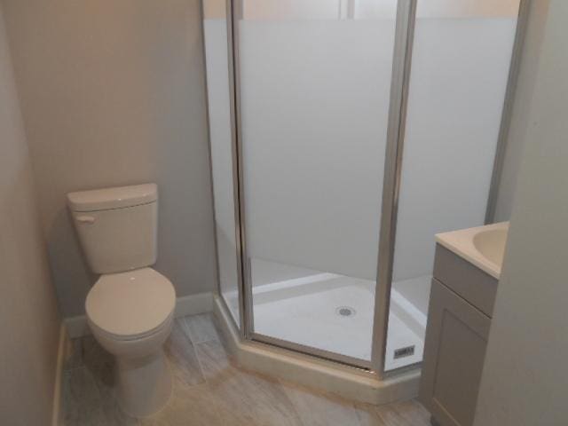 full bathroom featuring a stall shower, baseboards, vanity, and toilet