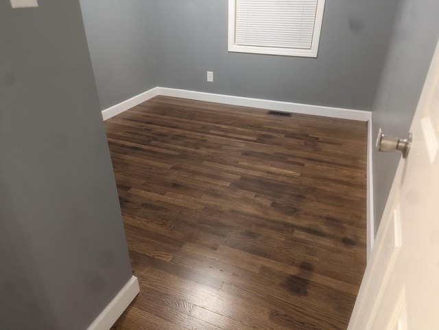 unfurnished room with dark wood-style flooring, visible vents, and baseboards