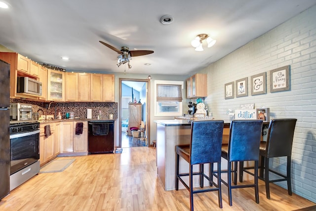 kitchen with a breakfast bar, black dishwasher, tasteful backsplash, oven, and light brown cabinetry