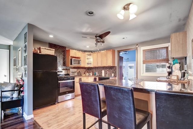 kitchen with kitchen peninsula, light wood-type flooring, tasteful backsplash, stainless steel appliances, and light brown cabinets