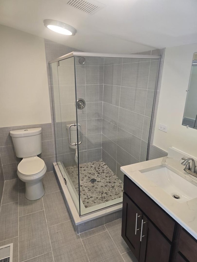 bathroom with an enclosed shower, vanity, tile walls, tile patterned flooring, and toilet