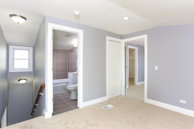 unfurnished bedroom featuring a closet, lofted ceiling, light tile patterned floors, and ensuite bath