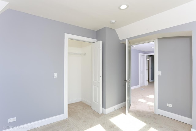 unfurnished bedroom featuring light carpet, vaulted ceiling, and a closet