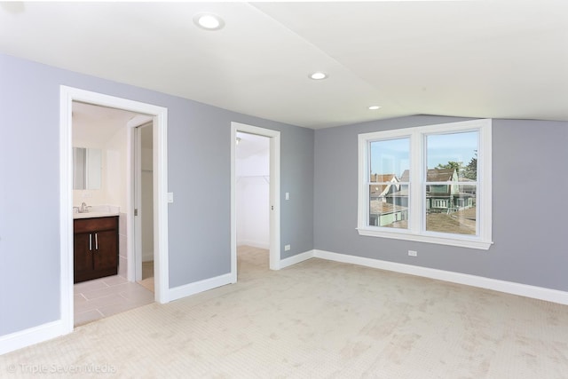 unfurnished bedroom featuring ensuite bath, light colored carpet, vaulted ceiling, a spacious closet, and a closet