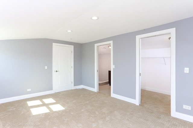 unfurnished bedroom with ensuite bathroom, a walk in closet, vaulted ceiling, light colored carpet, and a closet