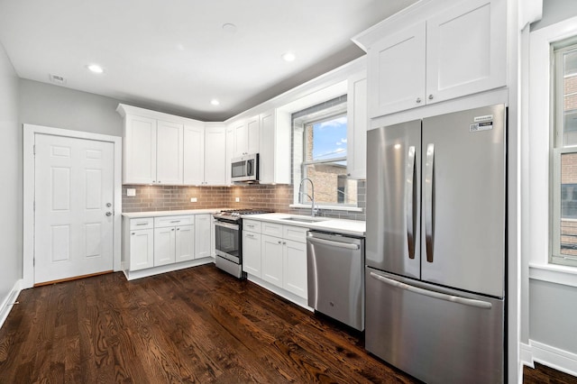 kitchen with appliances with stainless steel finishes, tasteful backsplash, white cabinetry, sink, and dark wood-type flooring