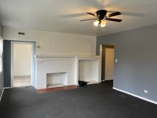 unfurnished living room with dark colored carpet, ceiling fan, and a fireplace