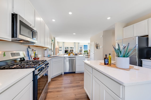 kitchen with appliances with stainless steel finishes, sink, white cabinets, a center island, and light hardwood / wood-style floors