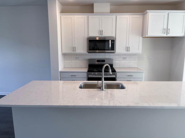 kitchen featuring tasteful backsplash, light stone countertops, white cabinets, and appliances with stainless steel finishes