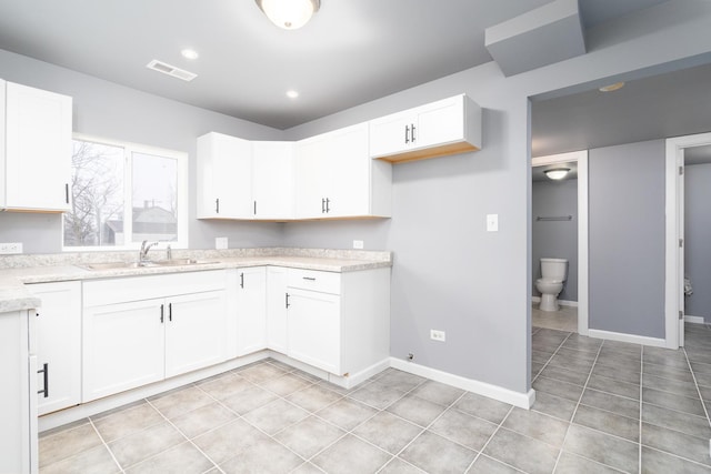 kitchen with white cabinetry, sink, light tile patterned flooring, and light stone counters