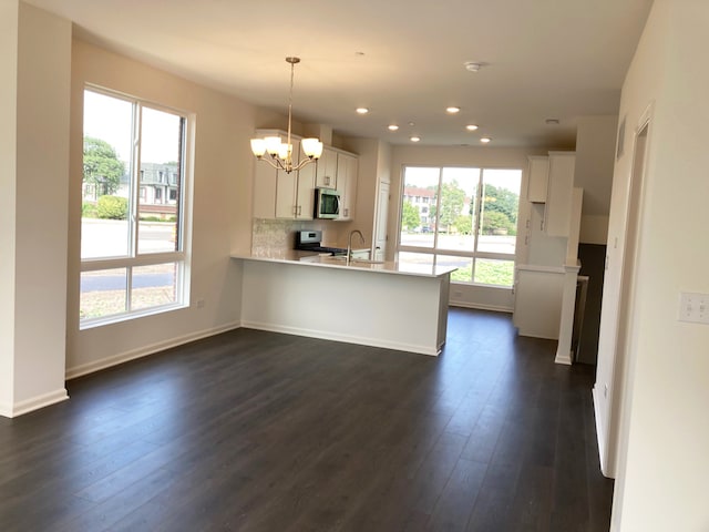 kitchen featuring dark wood-type flooring, range, white cabinets, hanging light fixtures, and kitchen peninsula