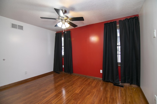 empty room with a textured ceiling, a healthy amount of sunlight, and dark wood-type flooring