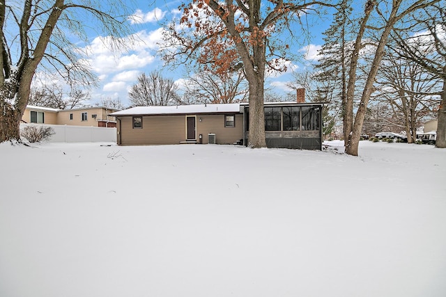 snow covered rear of property with a sunroom and central AC unit