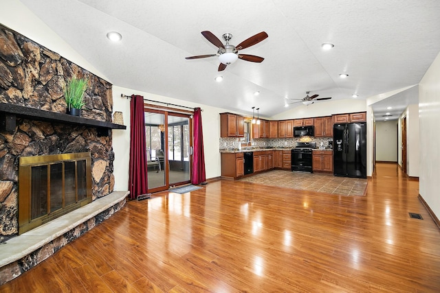 unfurnished living room with a stone fireplace, ceiling fan, vaulted ceiling, and light wood-type flooring