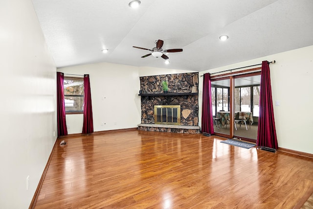 unfurnished living room with a wealth of natural light, vaulted ceiling, ceiling fan, wood-type flooring, and a stone fireplace