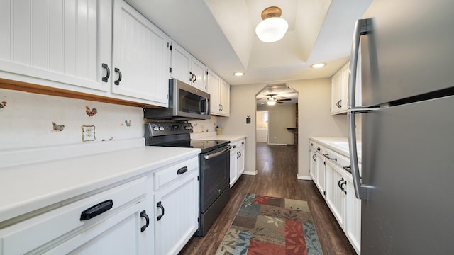 kitchen with dark hardwood / wood-style flooring, stainless steel appliances, a tray ceiling, ceiling fan, and white cabinetry