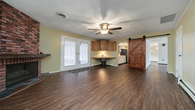 unfurnished living room with ceiling fan, a baseboard radiator, a brick fireplace, a barn door, and dark hardwood / wood-style floors