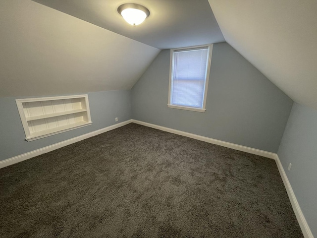 additional living space featuring dark carpet, vaulted ceiling, and built in features