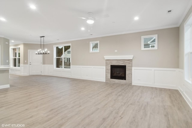 unfurnished living room featuring ceiling fan with notable chandelier, light wood-type flooring, ornamental molding, and a tiled fireplace