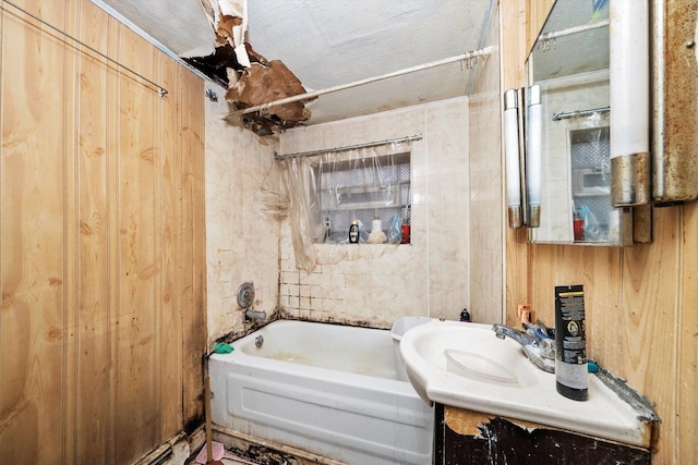 bathroom with a textured ceiling, vanity, wooden walls, and tub / shower combination